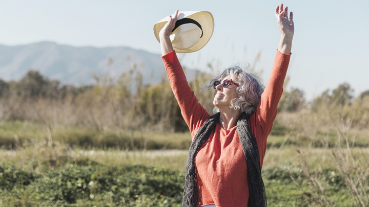 An older woman raising her hands in a happy gesture in the nature