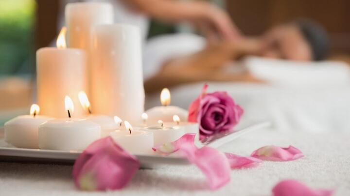 White candles burning on a plate, pink roses scattered next to it