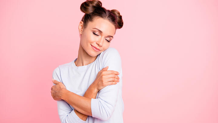 Young woman hugging herself in front of a pink background