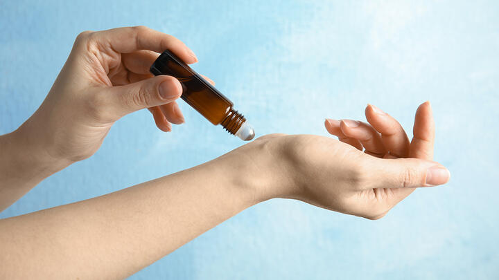 Woman's hands applying essential oil on her wrist against a light blue background