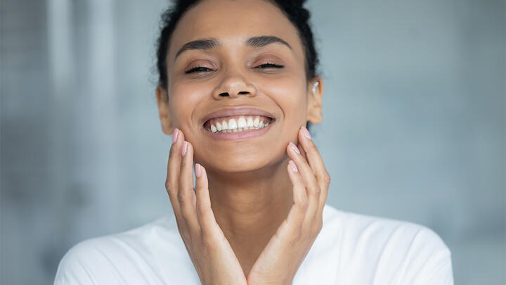 Young woman smiling, her hands pressed to her cheeks