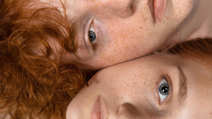 Two young models lying in bed cheek to cheek 