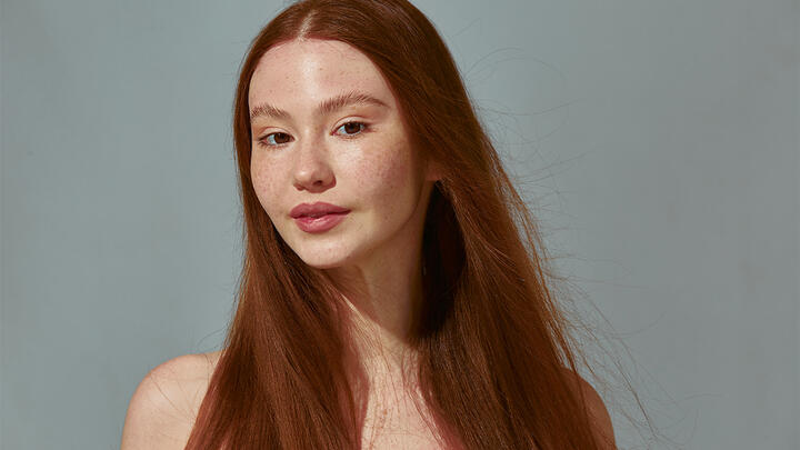 Young woman with long hair and freckles in front of a grey background