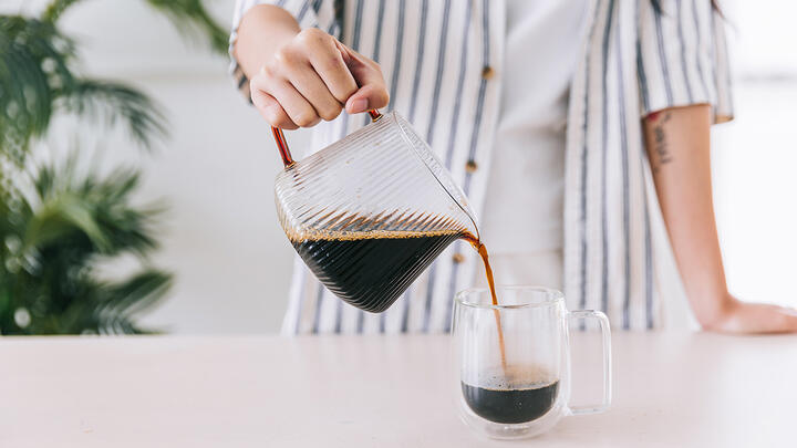 Closeup of a barista pouring coffee from a glass jug to a glass