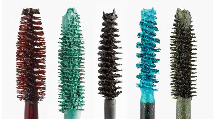 Colored mascara brushes isolated on black surface. From left to right: burgundy, green, brown, turquoise, golden