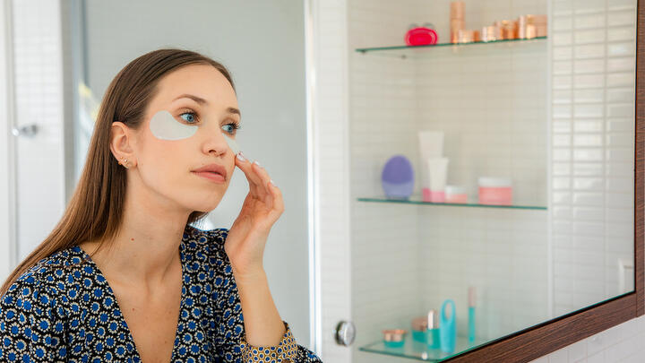 Young model with under-eye patches in a bathroom in front of a mirror