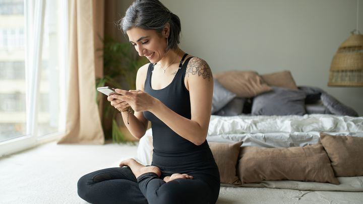 Woman in yoga pose in a bedroom holding a phone