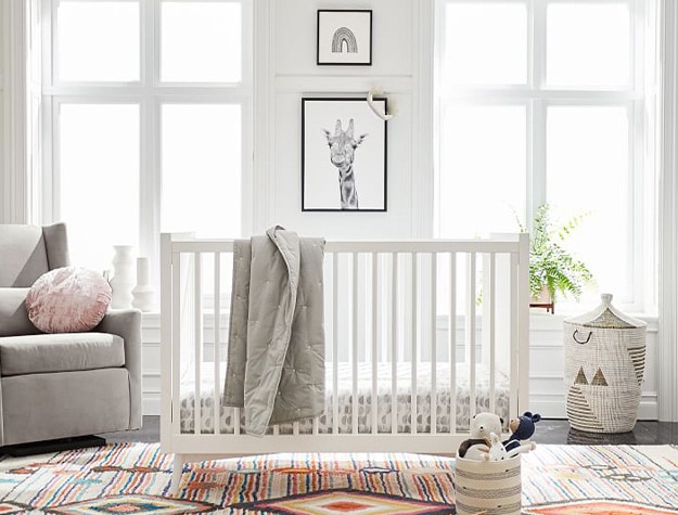 Black and white rainbow and giraffe prints above crib with rainbow rug below. 