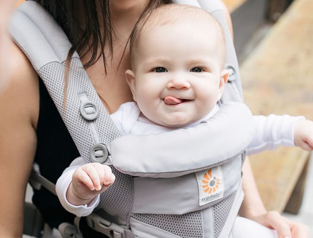 Mother with child strapped inside of baby carrier on her chest.