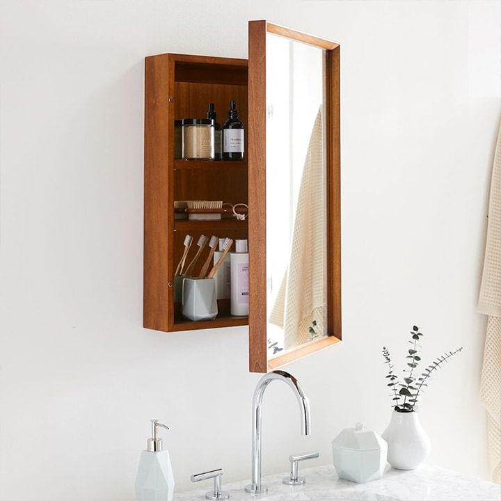 Wooden mid-century medicine cabinet with mirror door ajar.