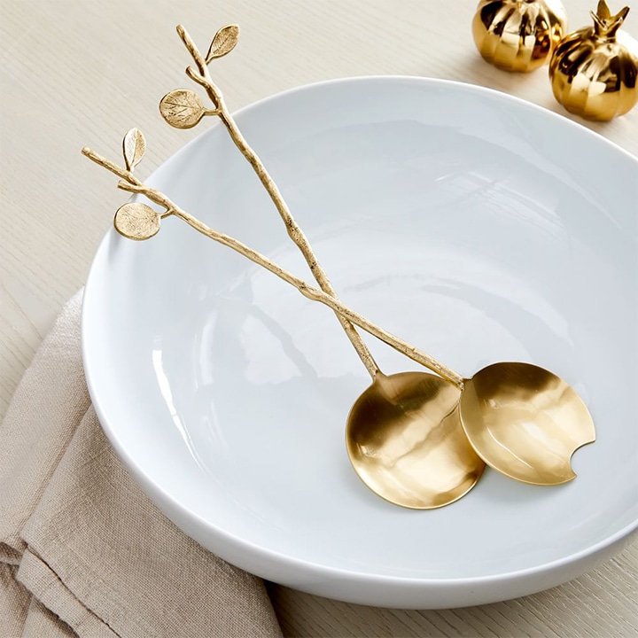 Gold botanical Salad servers on white bowl.