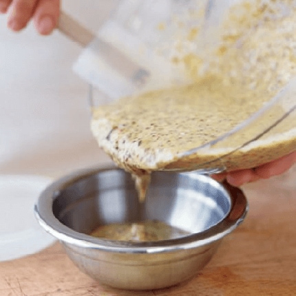 Mustard and rosemary barbecue sauce being poured into a silver bowl.