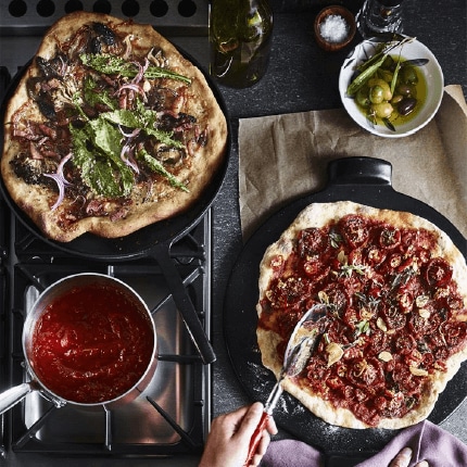 Set of pizzas one on a pizza stone and one in a frying pan.