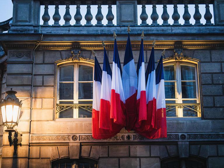 Französische Flaggen an der Fassade des Elysee-Palastes im Abendlicht.