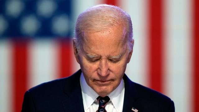 US-Präsident Joe Biden blickt nach unten. Hinter ihm ist die Flagge von den USA. 