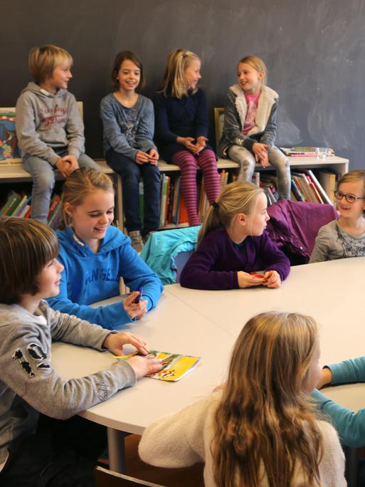 Kinder in einem Kinderparlament an einer Schule sitzen an einem runden Tisch, die Klassensprecherinnen treffen sich und besprechen verschiedene Probleme.