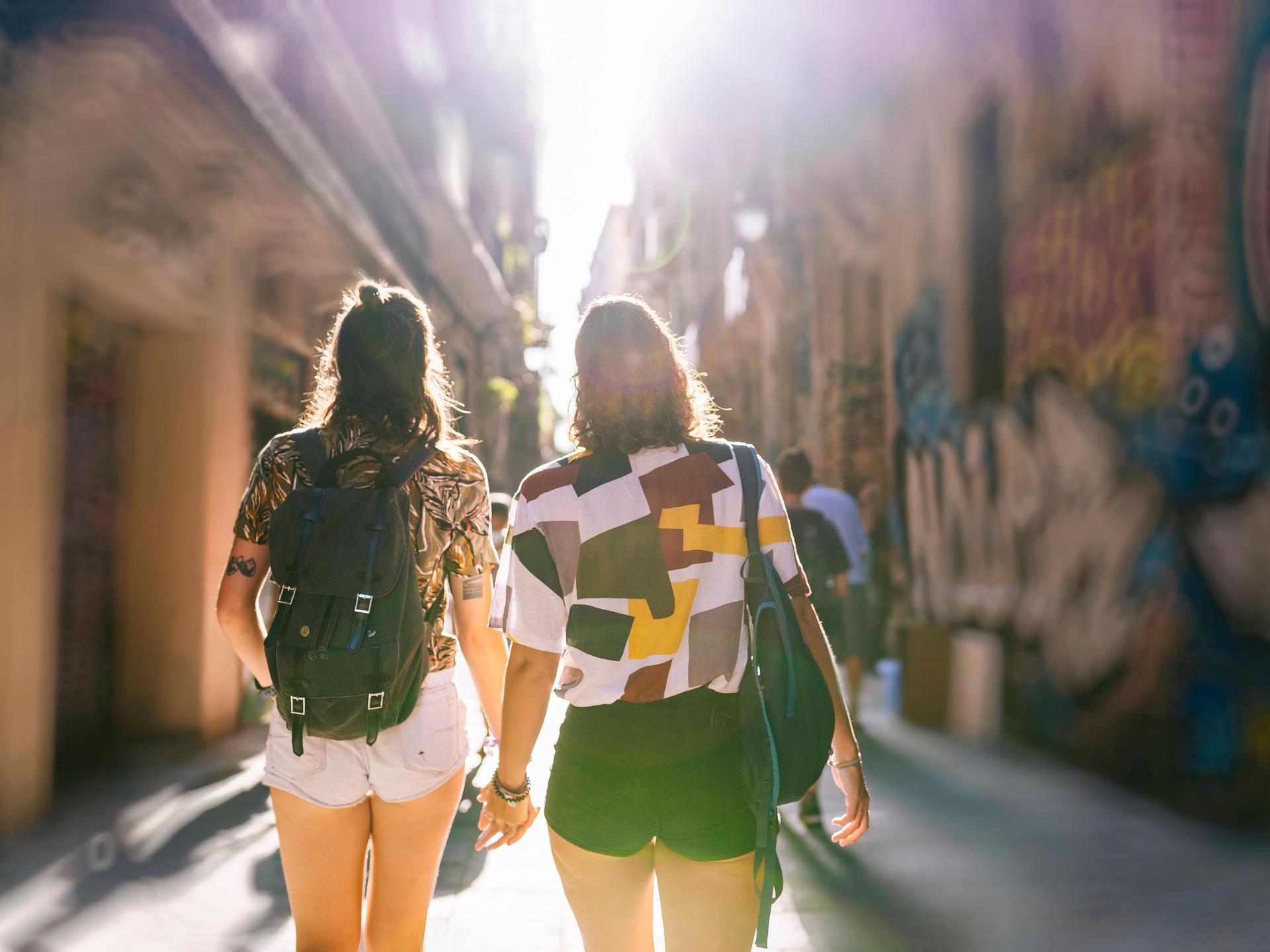 Zwei Frauen laufen Hand in Hand durch eine Gasse in einer sommerlichen Altstadt.