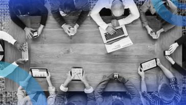 A conference table surrounded by people working on laptops and mobile devices