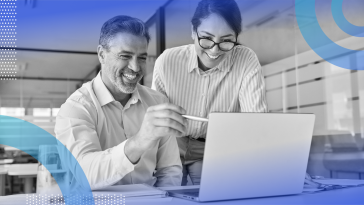 A man and a woman are looking at a computer screen and are smiling.