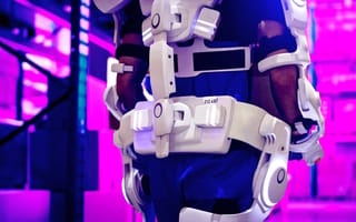 A person carrying boxes with the support of an exoskeleton on their back and limbs.