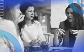 Talent management image of a dark haired woman listening to another woman explain a concept to a third light-haired woman across the table.