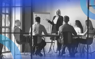 chief human resources officer a group of professionals in a meeting room. A white-haired woman in a skirt suit stands and gives a presentation to the gorup.