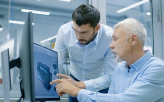 Two men at a desk work together on a product design displayed on a computer screen.