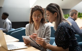 A rotational program participant and colleague sit next to each other going through a notepad.