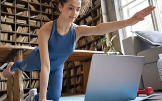 An employee holds a yoga pose as they watch a virtual fitness class on their laptop to illustrate a company wellness program.