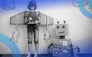 A child wearing cardboard wings and aviator goggles stands next to a smiling cardboard robot