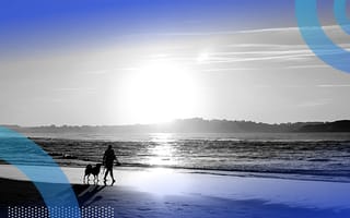 A woman walking her dog on a beach.