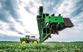 John Deere equipment working on a field beneath a cloudy sky