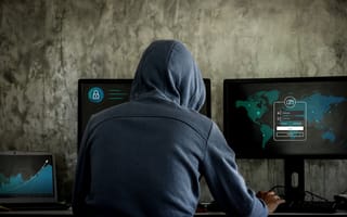 A photo of a person in a hoodie in front of computer monitors.