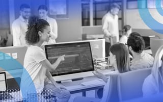 Software developers at an office are gathered around a large computer screen.