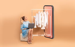 Woman Shopping Online Using Laptop Sitting Near Big Smartphone Choosing Clothes On Rail Over Beige Studio Background.