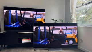 The LG G4 OLED TV on a TV bench, with LG G3 OLED next to it on the floor, and both showing the same scene of Dua Lip in the movie Argylle