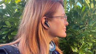 Earfun Air Pro 3 worn in the ears of a woman outdoors on wooden table