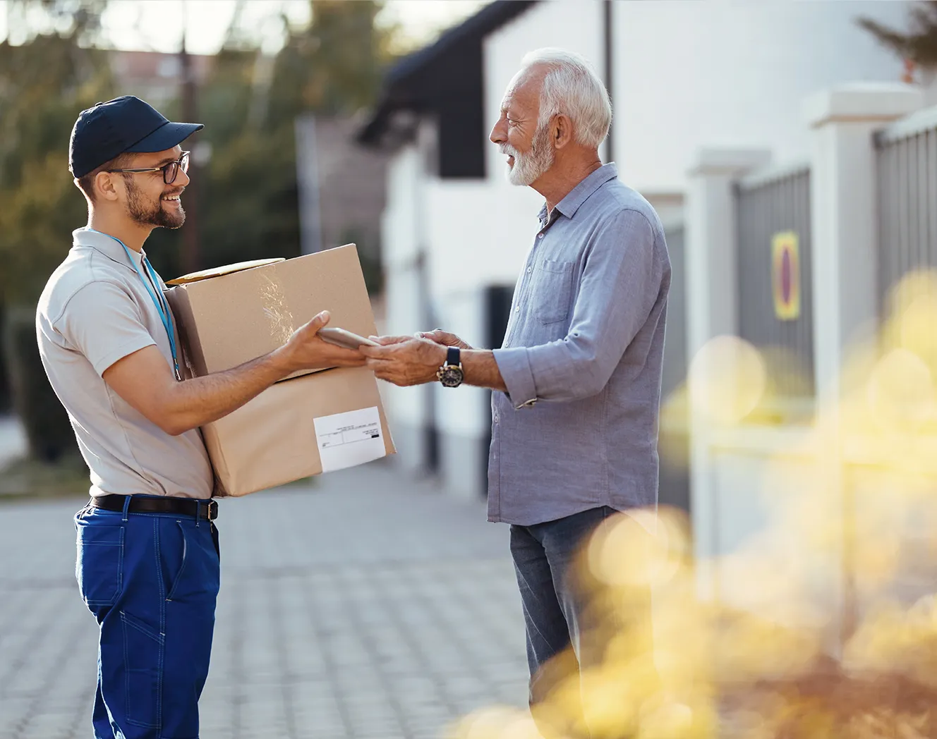 A young smiling courier delivering a parcel to an older gentleman with white beard and hair. Photo.