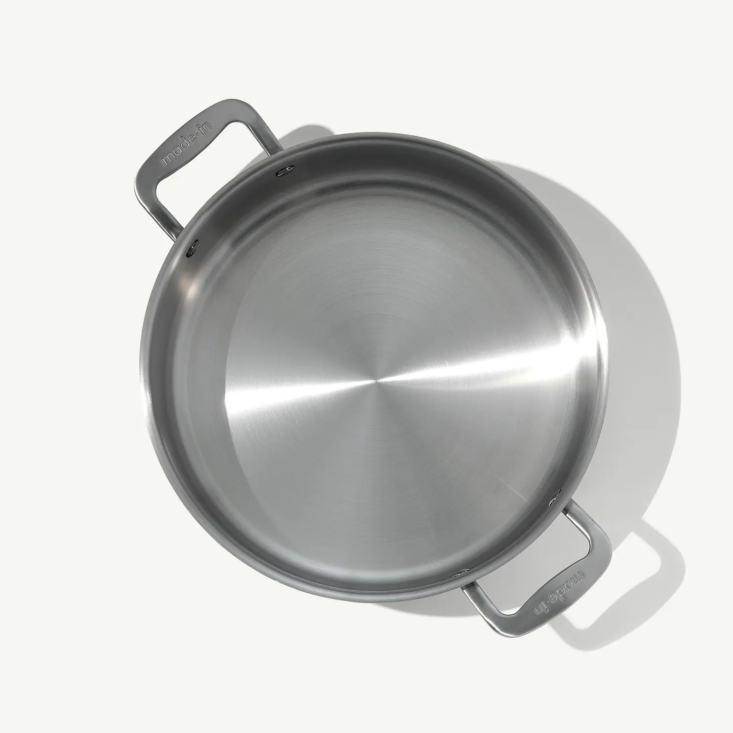 A stainless steel cooking pot with two handles is shown from above on a light background, casting a soft shadow.