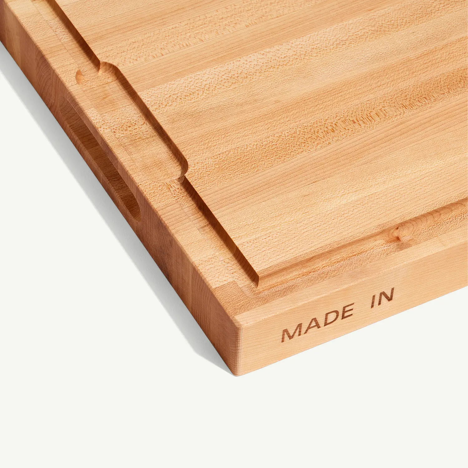 A wooden cutting board with the words "MADE IN" engraved on the side edge.