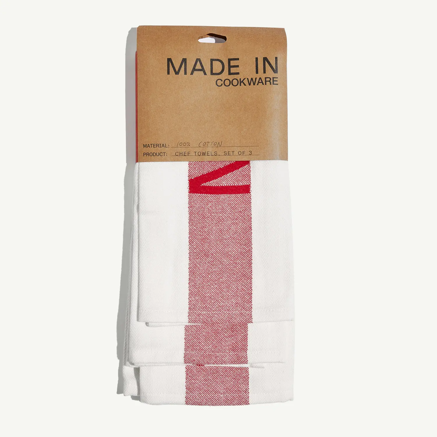 A set of neatly folded white kitchen towels with red stripes, packaged with a brown "MADE IN Cookware" label.