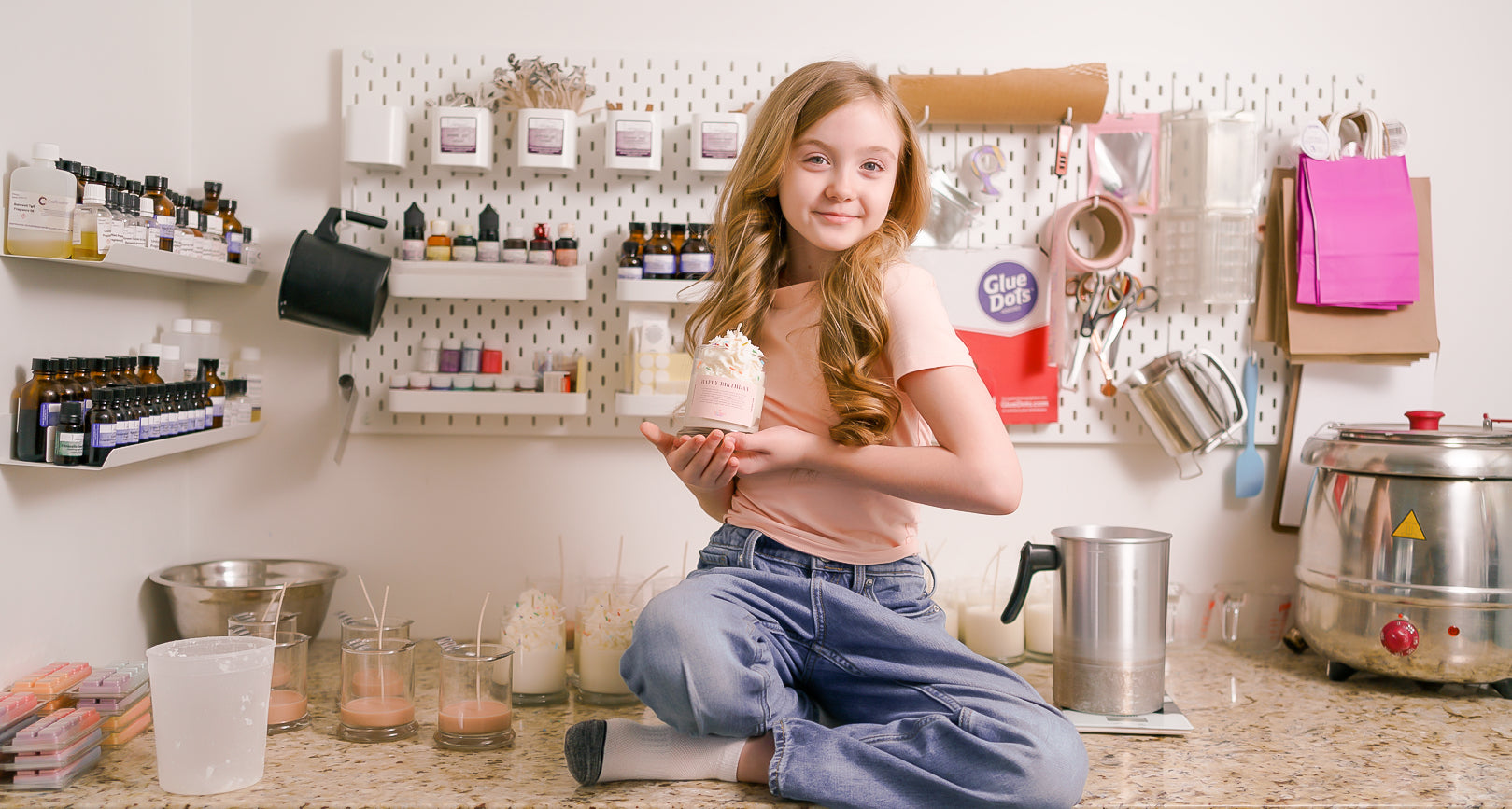 A kid sits on a counter holding a glass jar candle