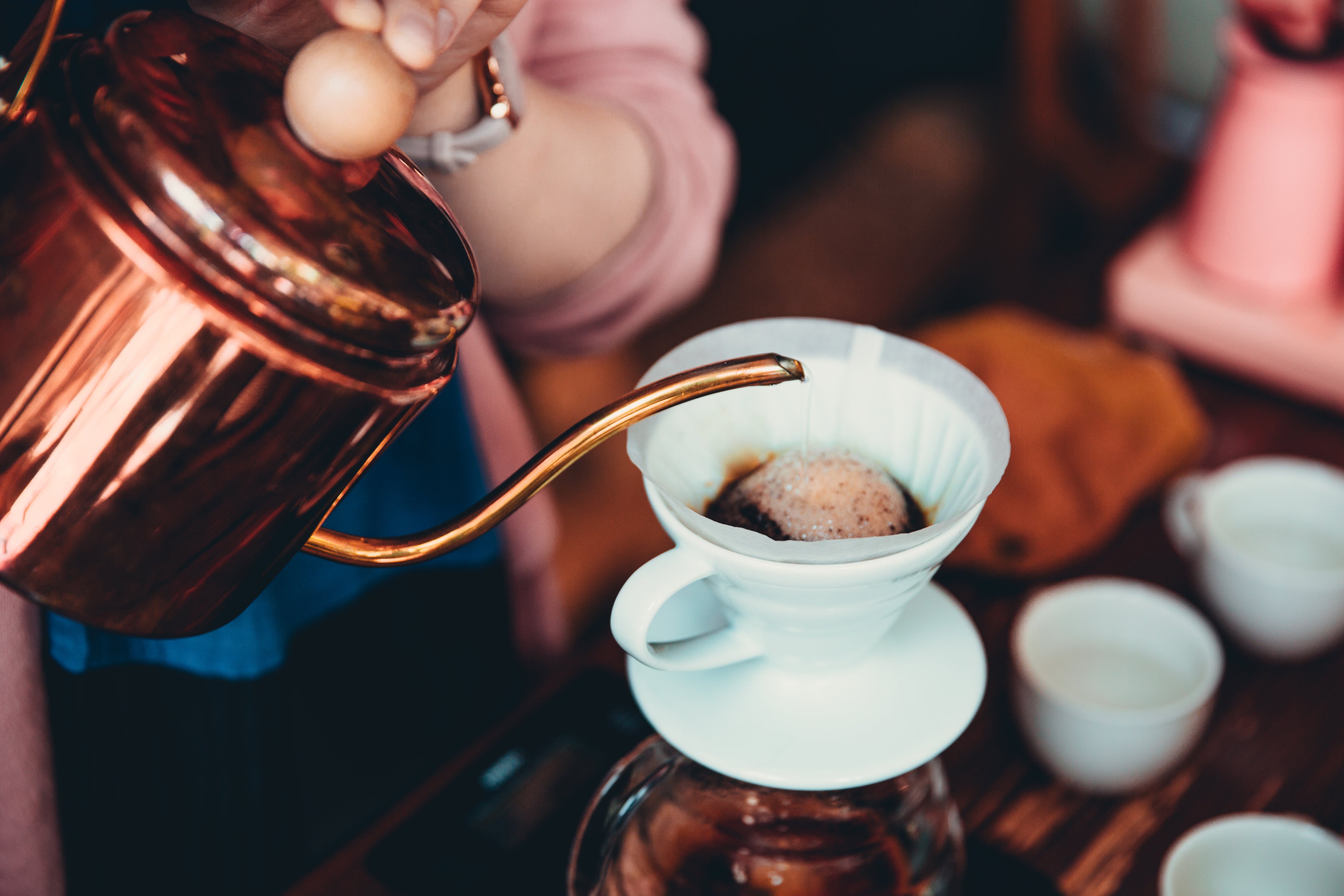 Lifestyle image of a hand pouring water from a copper kettle into a pourover coffee maker