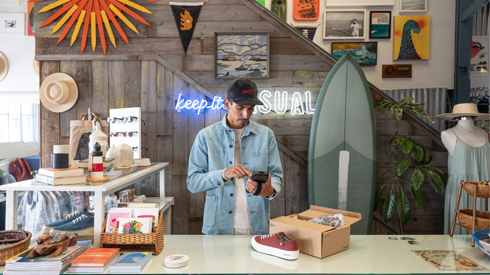 Checkout area of a retail store with a surfboard, LED sign, and artwork on the wall behind.