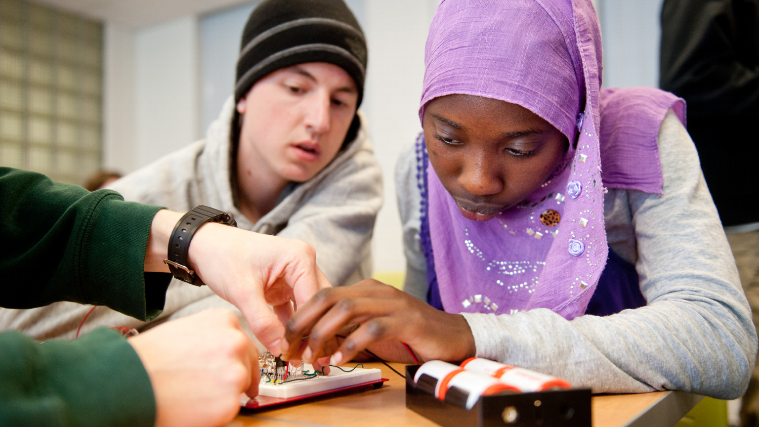 Two young students closely examine a device in a classroom setting.