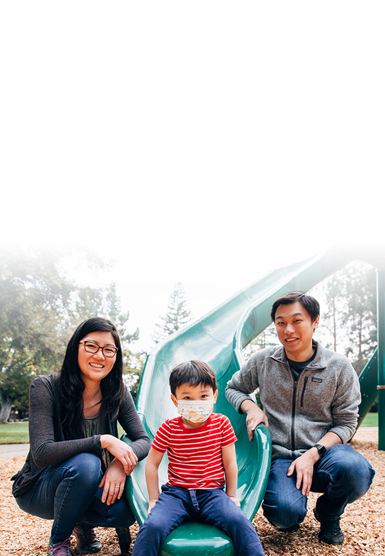 A women, child and man pose for a family picture at the foot of a playground slide.