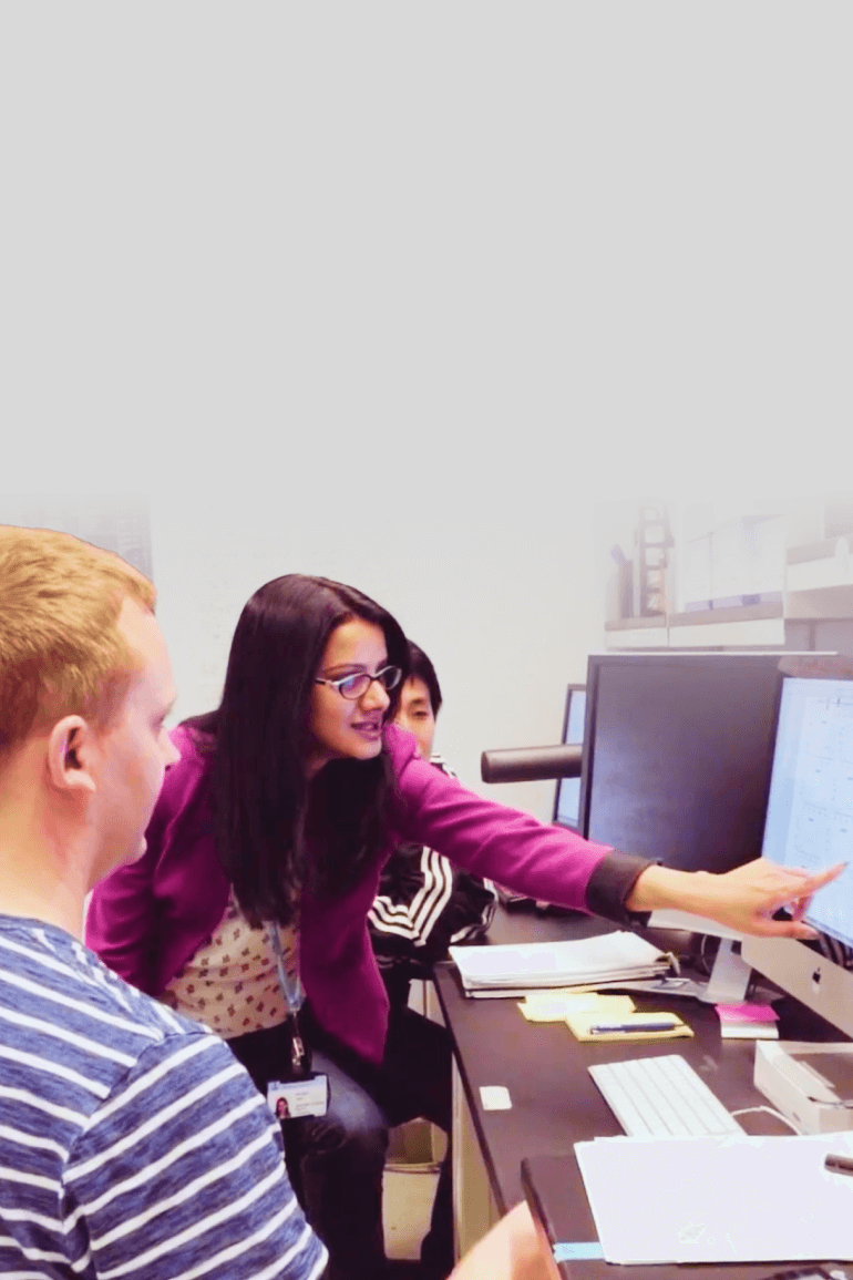 A group of researchers gathers around a computer. One researcher points at the computer screen.