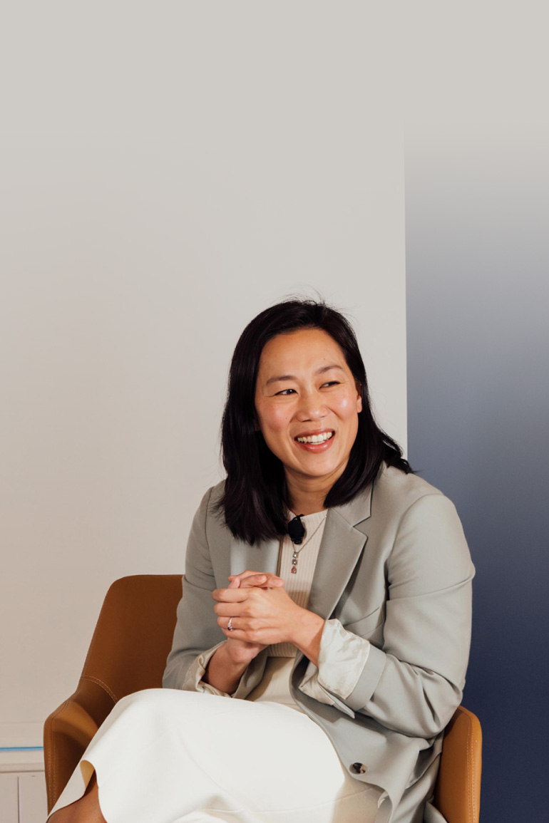 Priscilla Chan sits in an armchair on stage and clasps her hands. She smiles out at the audience.