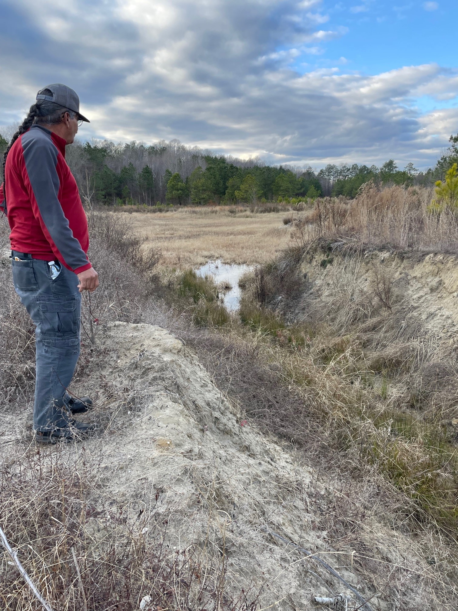 A man in a red and gray shirt stands looking at land.