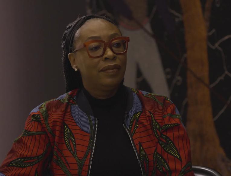 The artist Otobong Nkanga wearing red framed glasses and a multi-coloured jacket